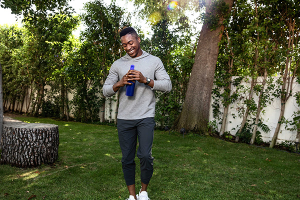 An athletic man with a blue water bottle smiles as he prepares to start his workout